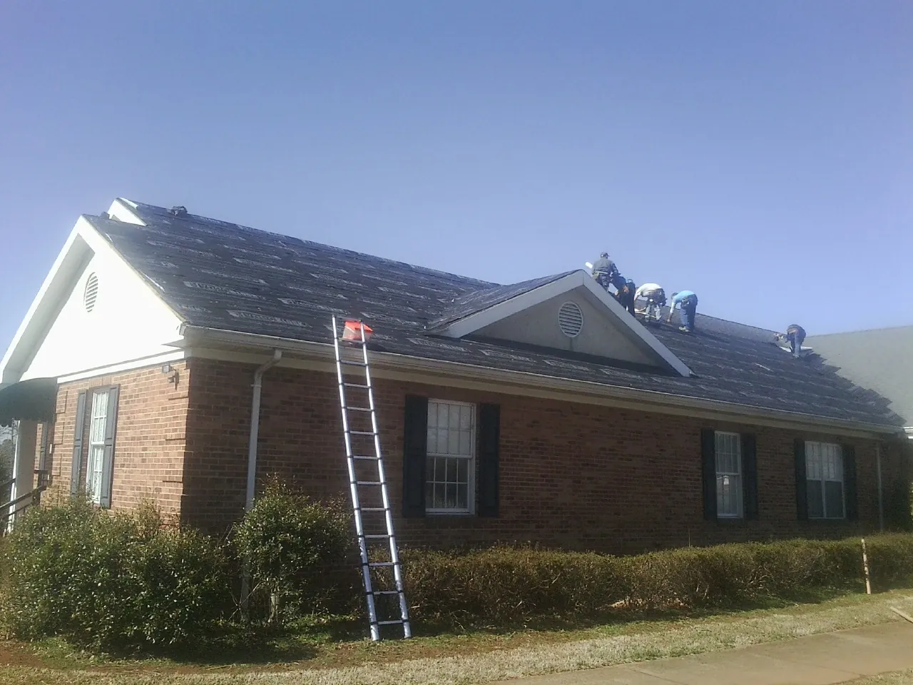 Crew tearing shingles off a brick ranch roof with a ladder set — Emergency Roof Repair work by our crew in Maple Shade