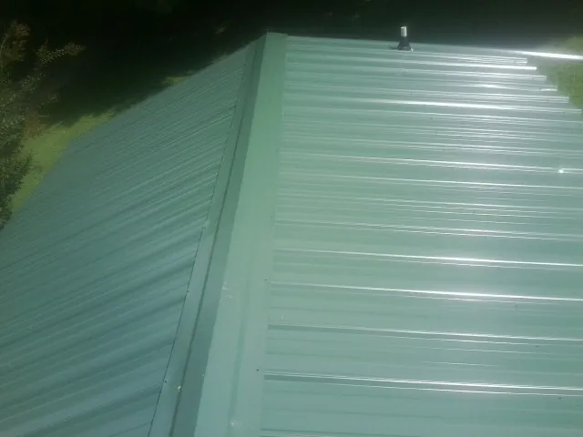New green metal panels meeting at the ridge of a roof — Flat Roof Repair work by our crew in Maple Shade
