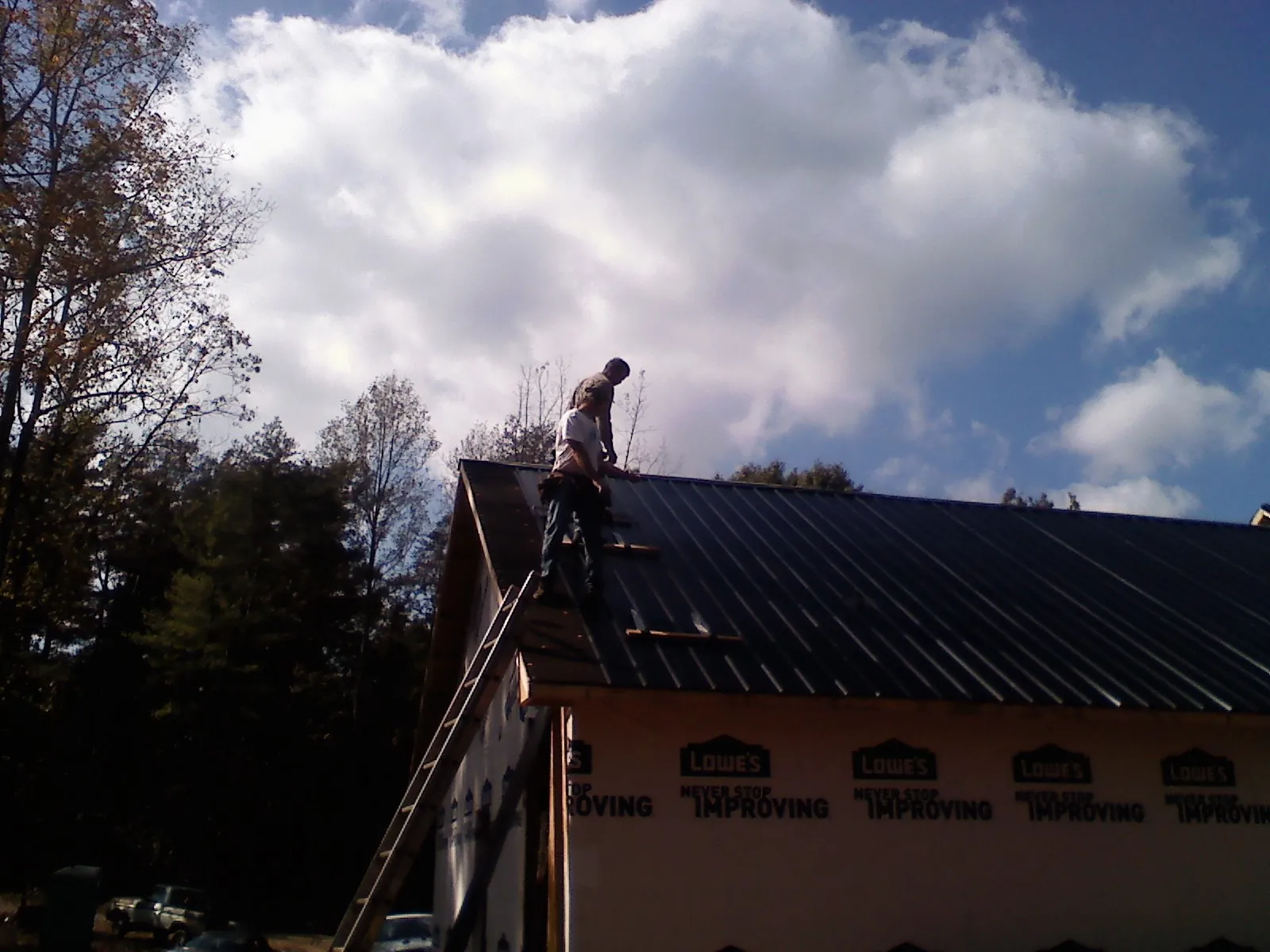 Roofer fastening dark metal panels high against a cloudy sky, from a Roof Inspection job in Maple Shade