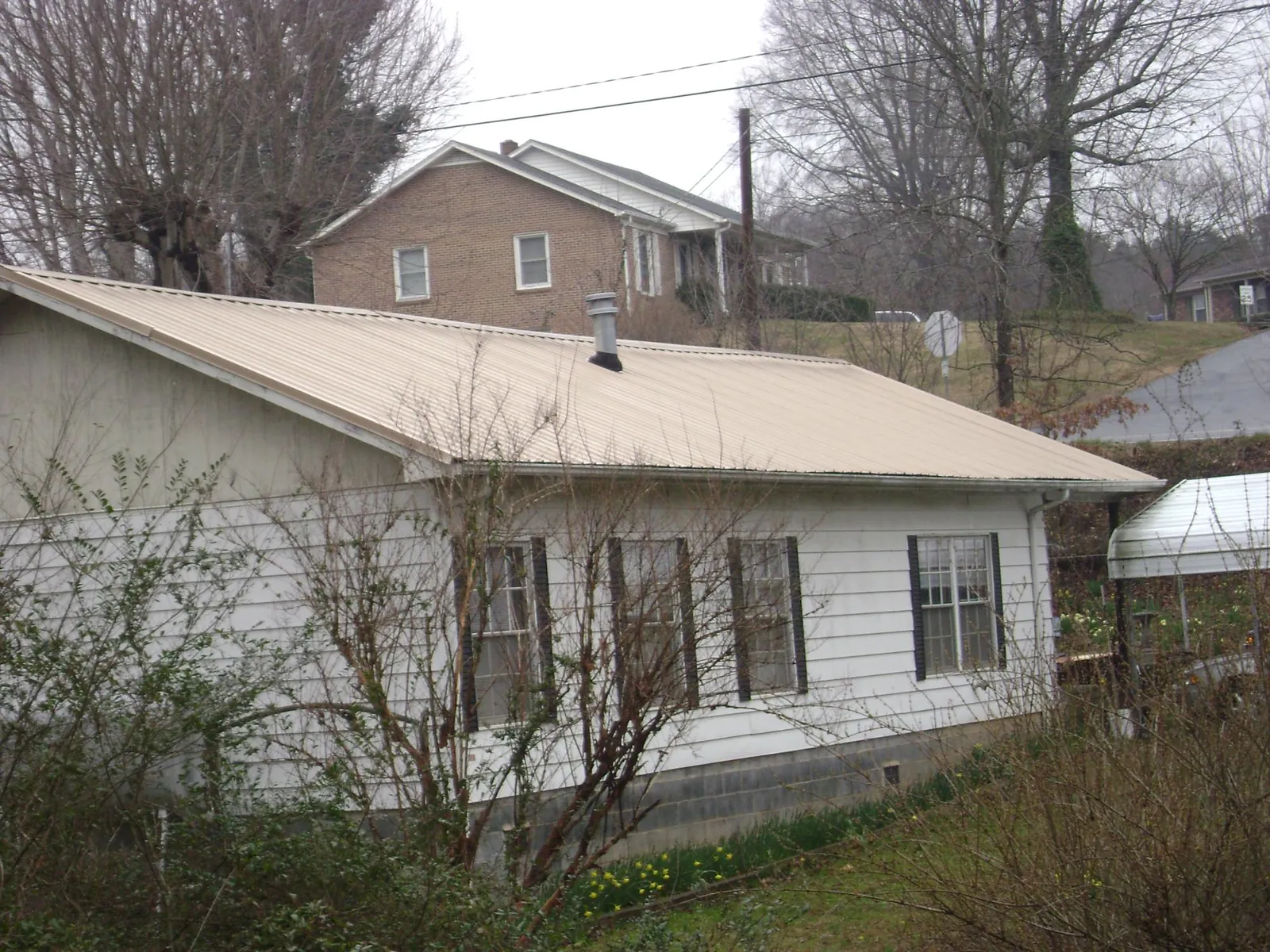 Tan metal roof on a white sided house set into a hillside — Commercial Roofing by Roofing Brothers in Maple Shade